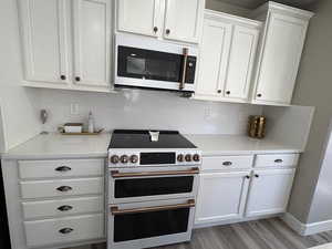 Kitchen with range with two ovens, tasteful backsplash, white microwave, and white cabinets