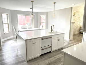 Gourmet kitchen with quartz countertops and table, a sink, 2 top-load dishwashers, light wood-style floors, and a wealth of natural light