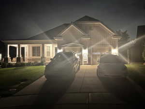 View of front of house featuring concrete driveway, stone siding, and a lawn