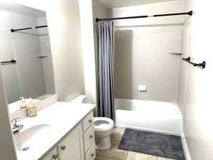 Downstairs bathroom featuring toilet, shower/bath combo with shower curtain, tile patterned flooring, and vanity