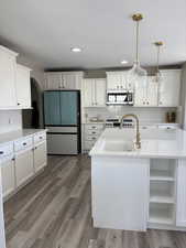 Kitchen with new Café fridge, microwave, large sink, white cabinets, and wood finished floors