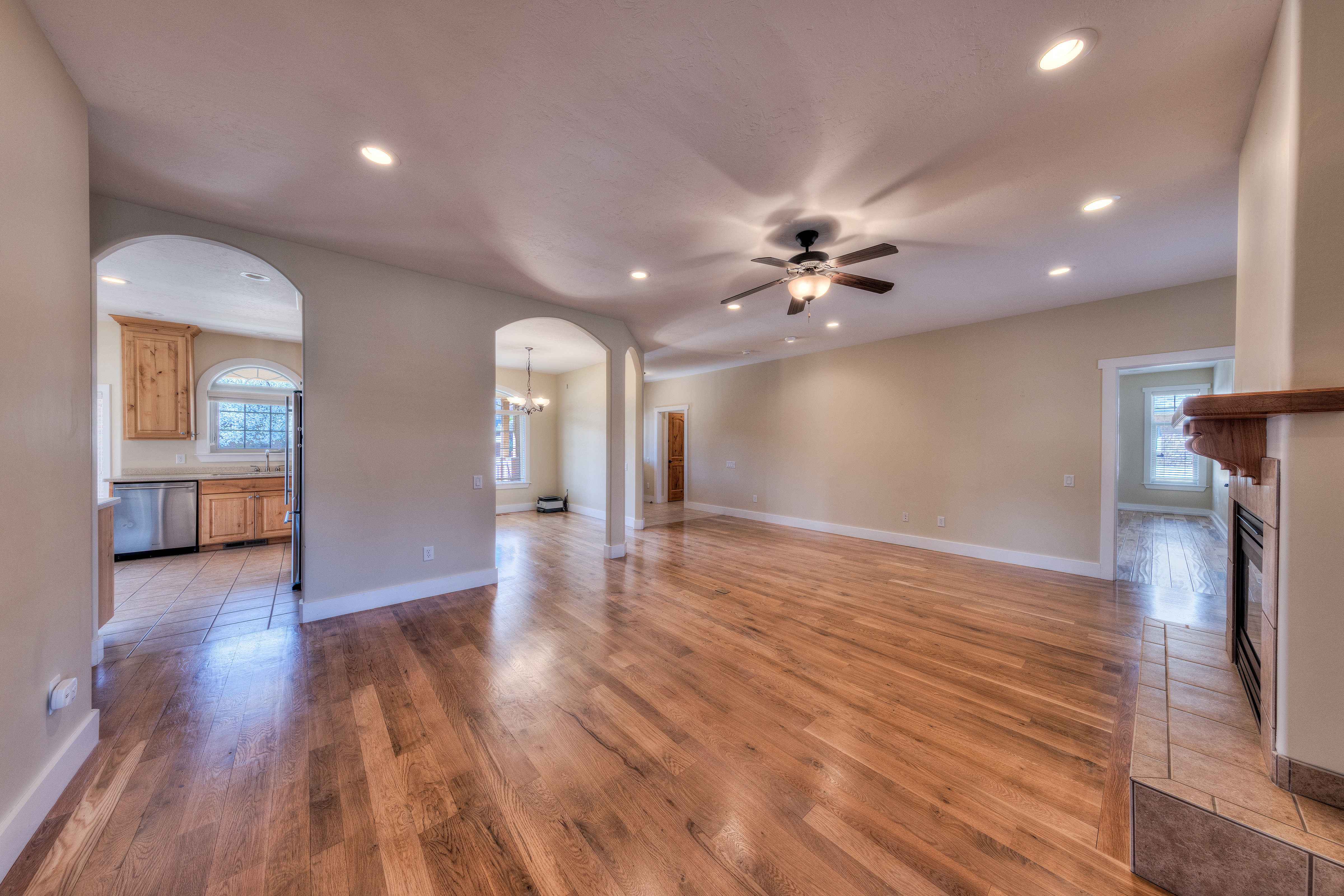 Unfurnished living room featuring recessed lighting, light wood-type flooring, ceiling fan with notable chandelier, arched walkways, and a glass covered fireplace