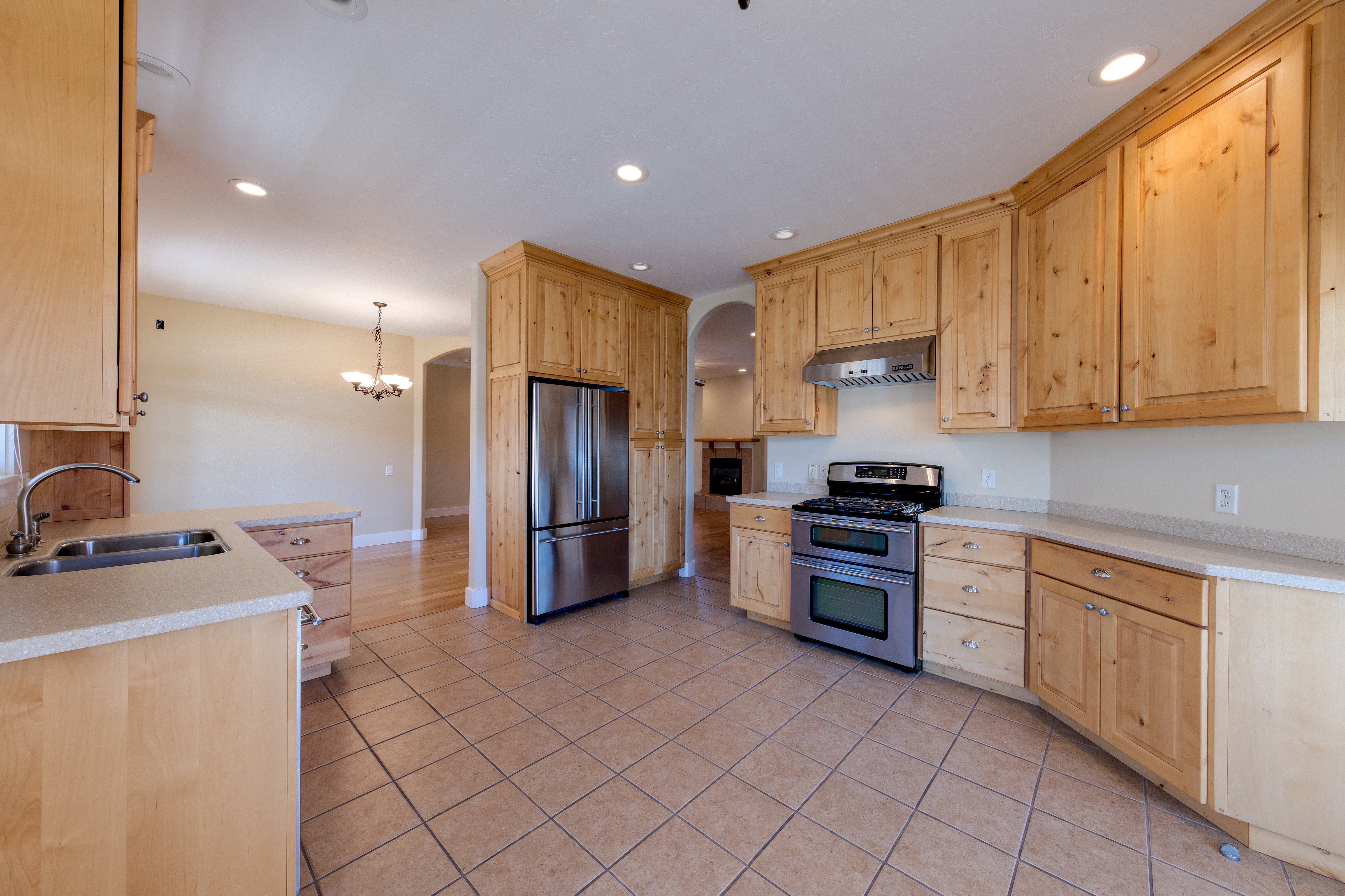 Kitchen featuring stainless steel appliances, light brown cabinets, under cabinet range hood, arched walkways, and a sink