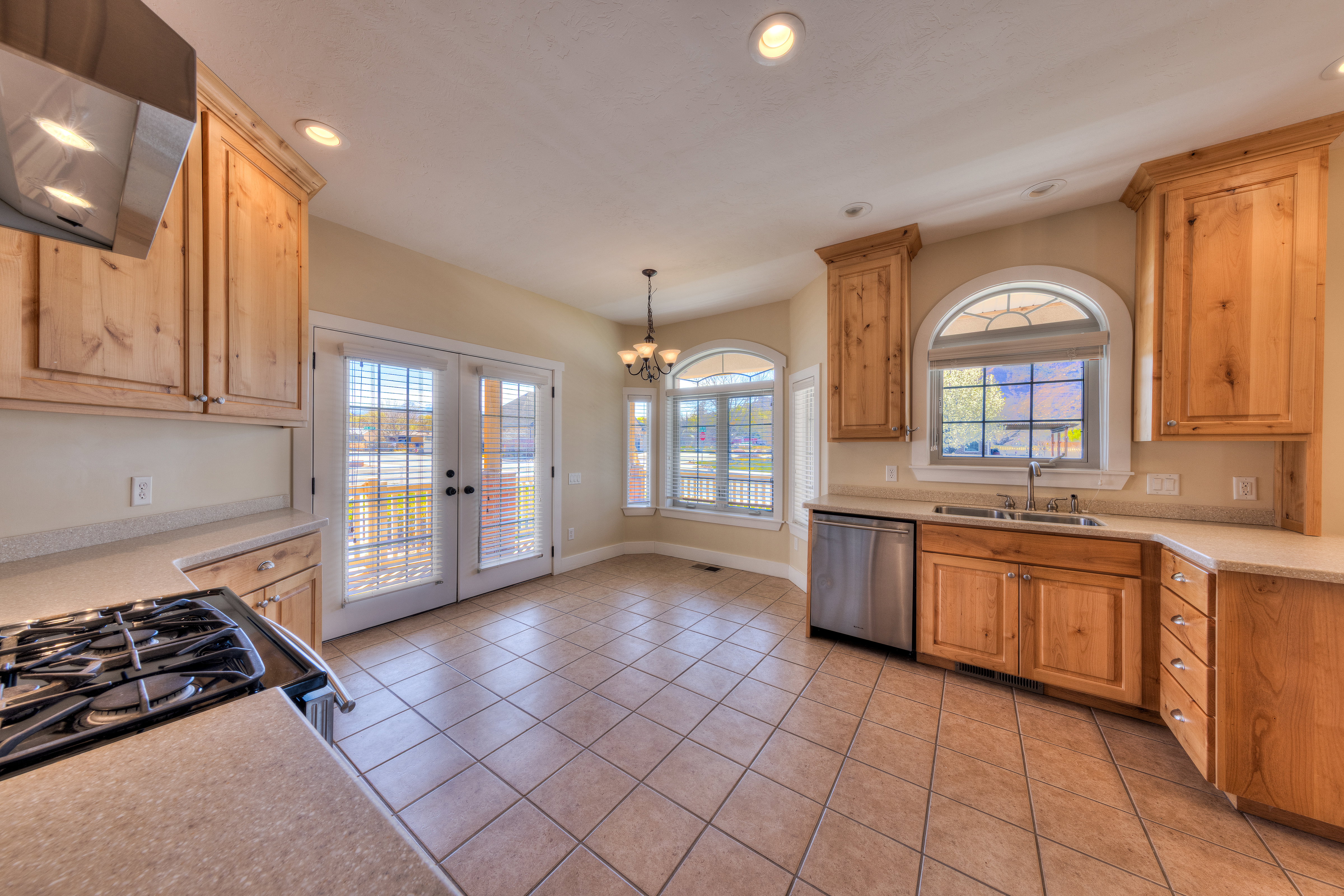 Kitchen with light countertops, a sink, a chandelier, wall chimney exhaust hood, and stainless steel dishwasher