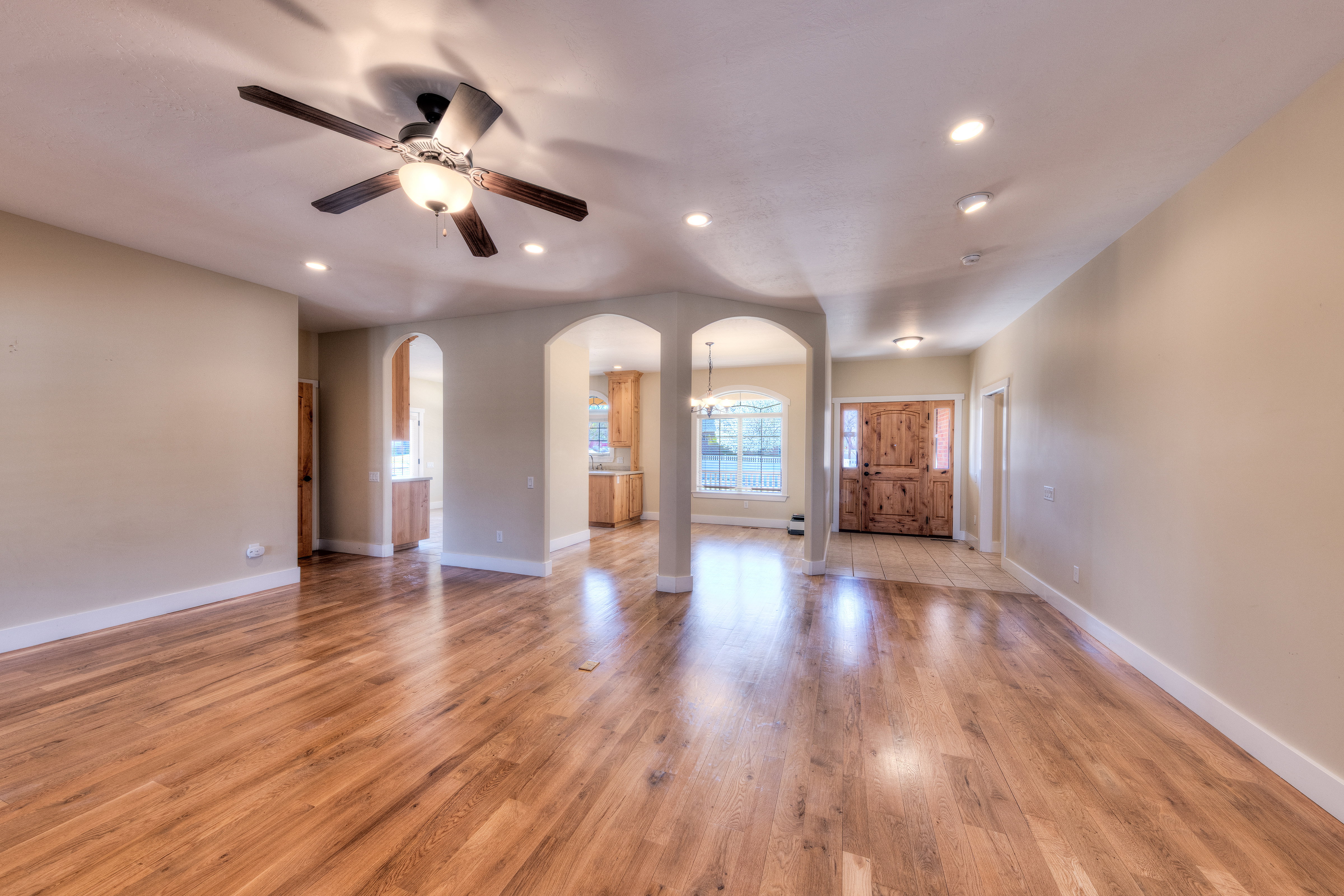 Unfurnished living room featuring light wood-style flooring, baseboards, arched walkways, and a ceiling fan