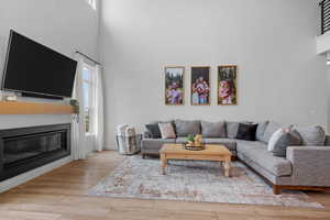 Living room with baseboards, a towering ceiling, a glass covered fireplace, and wood finished floors