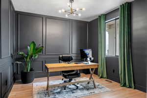 Office space featuring a decorative wall, a notable chandelier, light wood-style flooring, and visible vents