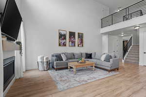 Living room with stairway, baseboards, a high ceiling, a glass covered fireplace, and wood finished floors