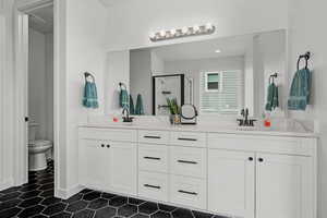 Bathroom featuring toilet, double vanity, a sink, and a stall shower