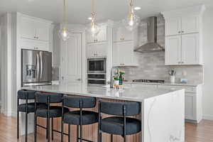 Kitchen with a sink, white cabinetry, tasteful backsplash, stainless steel appliances, and wall chimney range hood