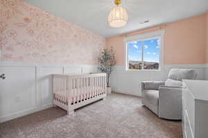 Carpeted bedroom featuring wallpapered walls, a wainscoted wall, a crib, and visible vents