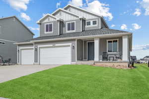 Craftsman house featuring an attached garage, board and batten siding, driveway, a front lawn, and covered porch