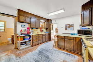 Kitchen with light countertops, open shelves, light wood-type flooring, stainless steel microwave, and a peninsula