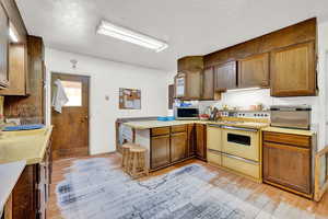 Kitchen with a sink, a peninsula, white range with electric cooktop, light wood-style flooring, and stainless steel microwave