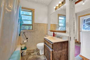 Full bath featuring vanity, shower / tub combo with curtain, tile walls, toilet, and a wainscoted wall
