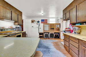 Kitchen with light countertops, freestanding refrigerator, a textured ceiling, range, and light wood-style floors