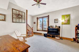 Sitting room featuring stairs, a textured ceiling, baseboards, ceiling fan, and carpet