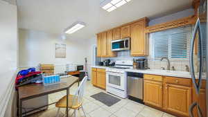 Kitchen with a sink, backsplash, brown cabinets, light tile patterned floors, and stainless steel appliances