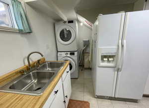 Laundry area featuring light tile patterned floors, a sink, laundry area, and stacked washer / drying machine