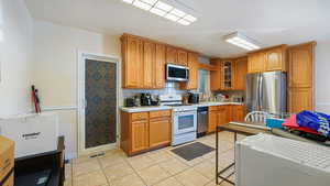 Kitchen with light countertops, light tile patterned floors, appliances with stainless steel finishes, and decorative backsplash