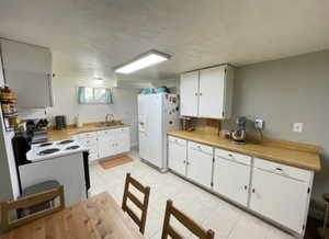 Kitchen with light countertops, a sink, white cabinetry, light tile patterned floors, and white appliances