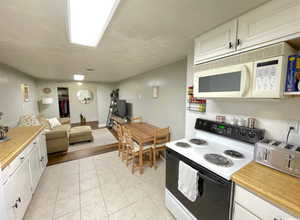 Kitchen with electric stove, light countertops, white microwave, and white cabinets