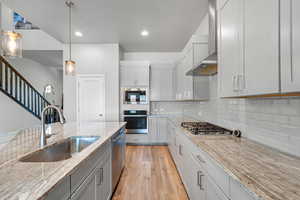 Kitchen featuring decorative backsplash, wall chimney exhaust hood, stainless steel appliances, a sink, and light wood-type flooring