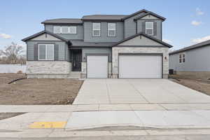 View of front facade with stone siding, an attached garage, driveway, and a shingled roof