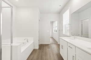 Full bath with wood finished floors, a bath, double vanity, baseboards, and a shower with door