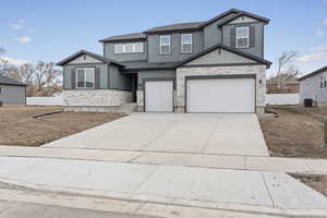 View of front of home with stone siding, a garage, concrete driveway, and fence