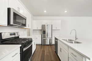 Kitchen featuring stainless steel appliances, a sink, dark wood finished floors, white cabinetry, and light stone countertops