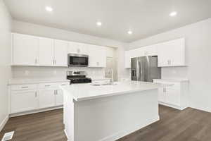 Kitchen with appliances with stainless steel finishes, a sink, white cabinetry, dark wood finished floors, and baseboards