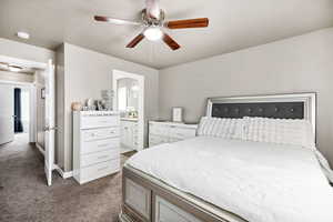 Bedroom with baseboards, dark colored carpet, ceiling fan, and ensuite bath