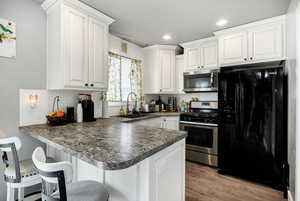 Kitchen with white cabinets, a peninsula, dark countertops, appliances with stainless steel finishes, and a sink