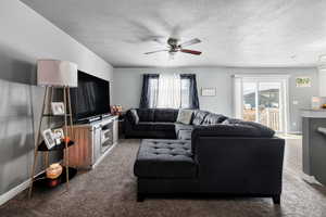 Carpeted living room with a textured ceiling, baseboards, and ceiling fan