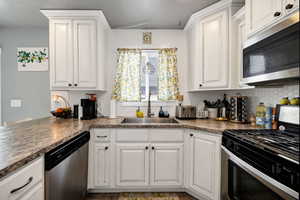 Kitchen featuring white cabinetry, stainless steel appliances, backsplash, a sink, and dark countertops