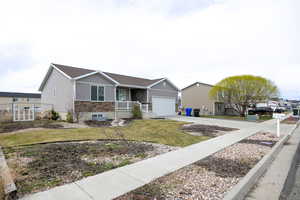 Ranch-style house featuring a front yard, covered porch, concrete driveway, fence, and an attached garage