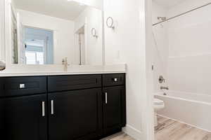 Full bath with washtub / shower combination, vanity, and wood finished floors