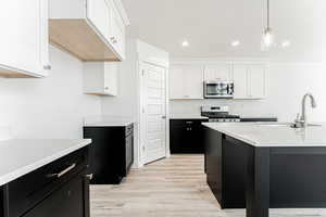 Kitchen featuring stainless steel microwave, range, dark cabinetry, light countertops, and white cabinets