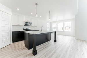 Kitchen with stainless steel microwave, range, a chandelier, light wood-type flooring, and light countertops