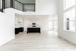 Unfurnished living room with a high ceiling, a chandelier, light wood-type flooring, and recessed lighting