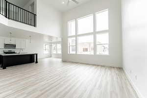 Unfurnished living room featuring a high ceiling, ceiling fan, and light wood-style flooring
