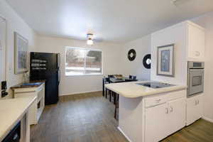 Kitchen with a peninsula, dark wood-style floors, white cabinetry, black appliances, and light countertops