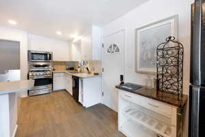 Kitchen with stainless steel appliances, white cabinetry, dark wood-style floors, recessed lighting, and light stone counters