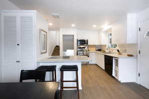 Kitchen featuring a peninsula, appliances with stainless steel finishes, a breakfast bar area, dark wood-style flooring, and light countertops