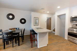 Kitchen with stainless steel appliances, light wood-style flooring, white cabinets, a kitchen bar, and recessed lighting