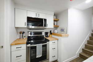 Kitchen with white cabinets, appliances with stainless steel finishes, open shelves, and wooden counters