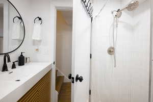 Bathroom featuring a tile shower, vanity, and dark wood-style floors
