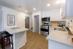 Kitchen featuring dark wood finished floors, stainless steel appliances, a kitchen breakfast bar, white cabinets, and recessed lighting