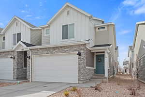 Townhome / multi-family property with stone siding, board and batten siding, concrete driveway, and an attached garage